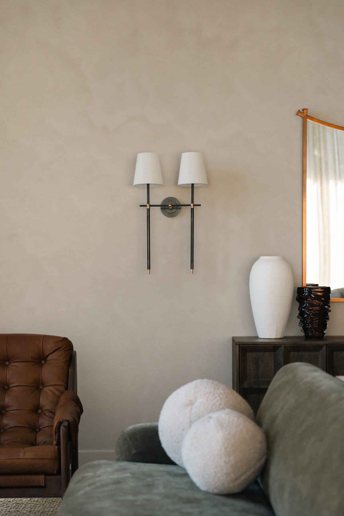 Devonshire Residence living room detail with dual wall sconces, dark credenza, white ceramic vase and layered seating in leather and velvet