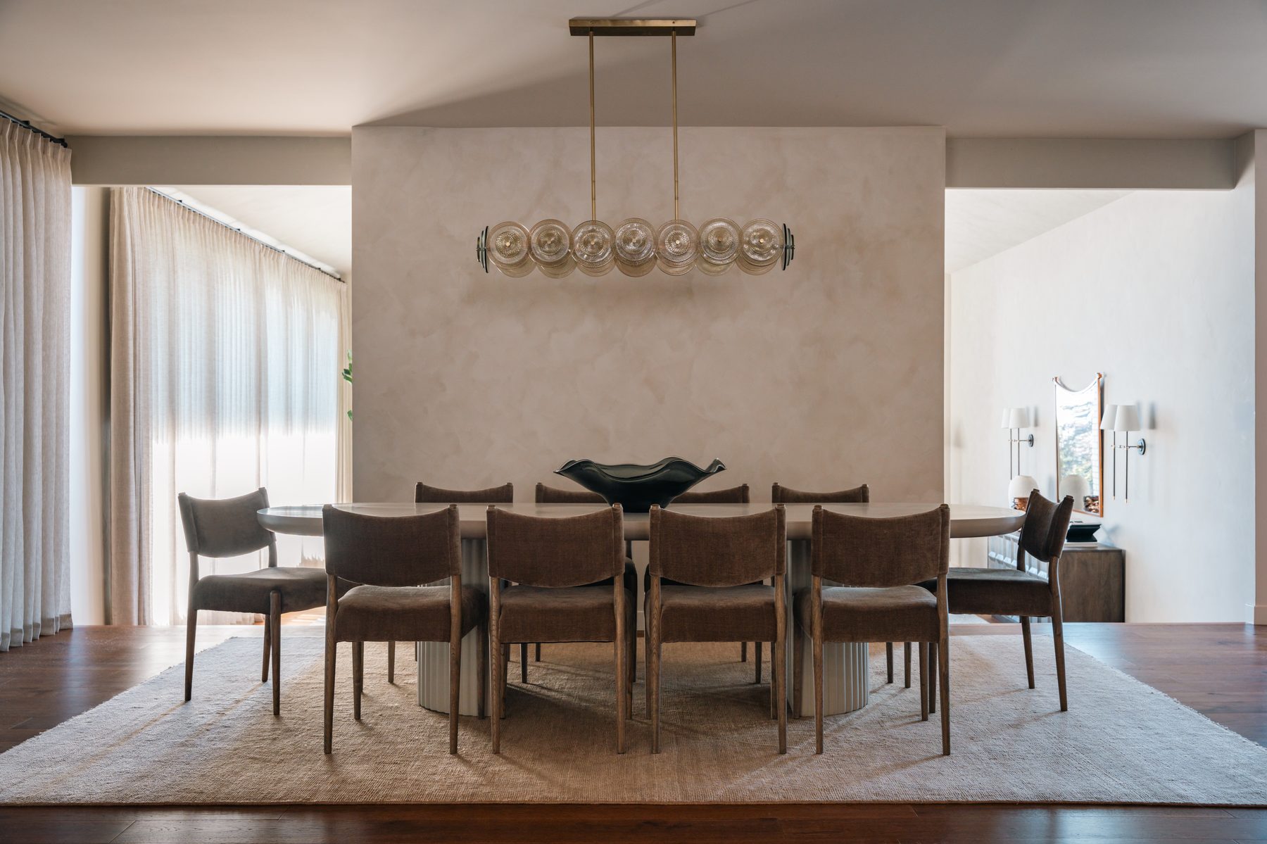 Devonshire Residence dining room with oval pedestal table, velvet chairs and smoked glass chandelier against limewashed wall, interior design by 7thandstone