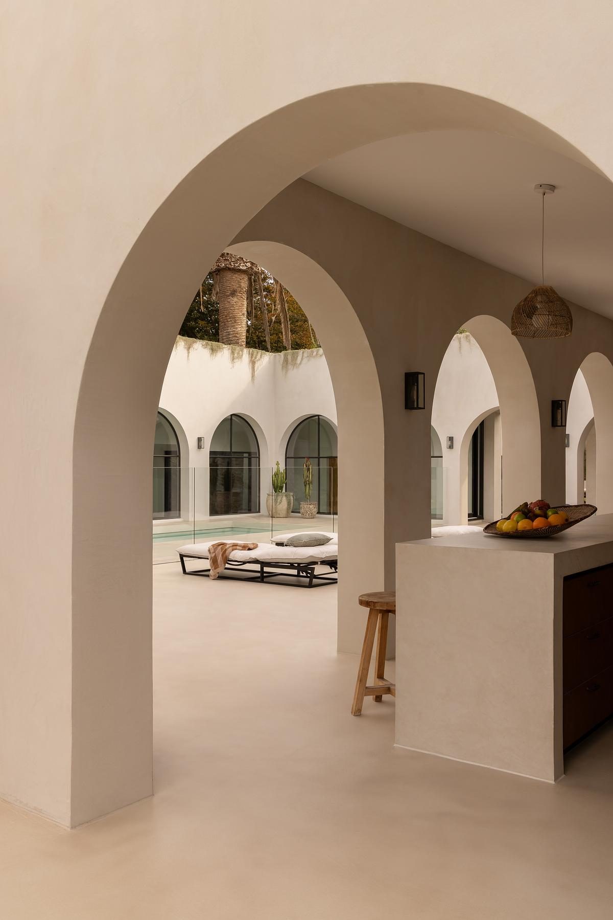A Coastal Alchemy courtyard, graceful rendered arches opening to the pool and palms beyond
