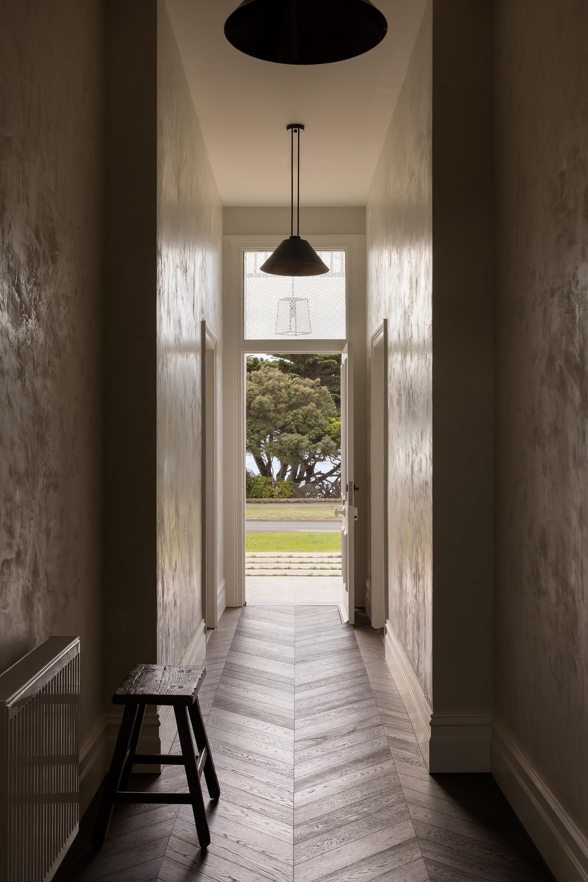 Entry corridor with herringbone timber floors, limewashed plaster walls and black pendant lights