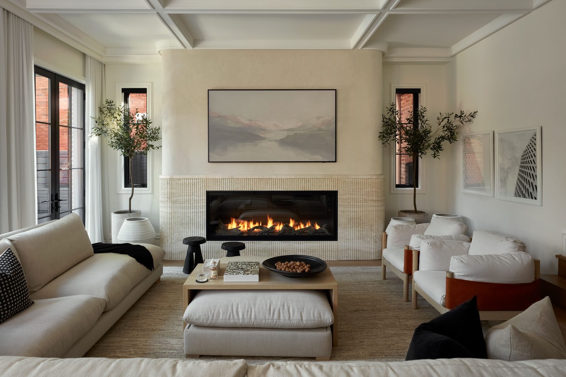 Midtown House living room with coffered ceiling, stone fireplace, olive trees and linen sofas