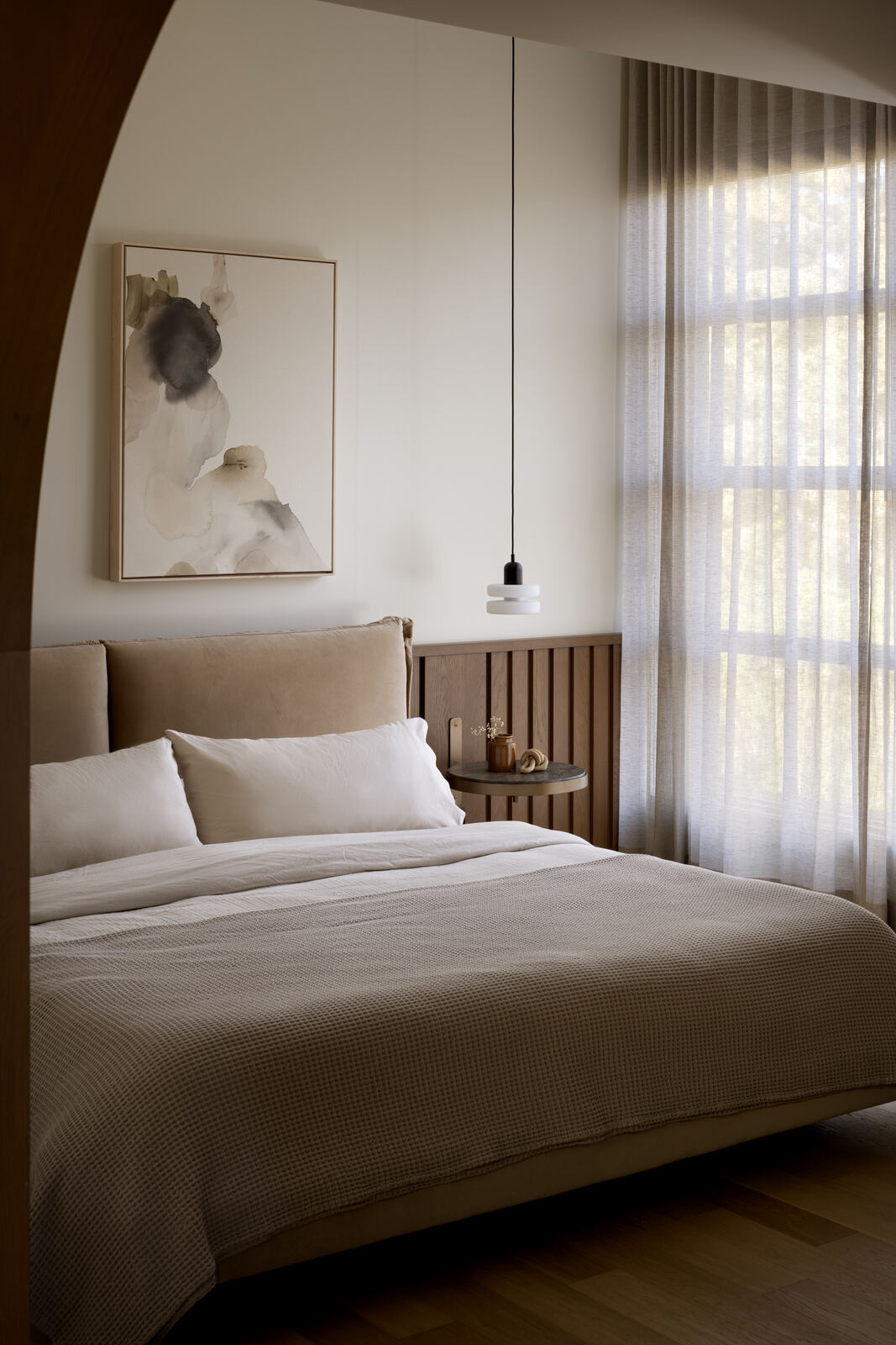 Bedroom with soft linen bedding and curved bedhead seen through an arched opening, Madison Residence