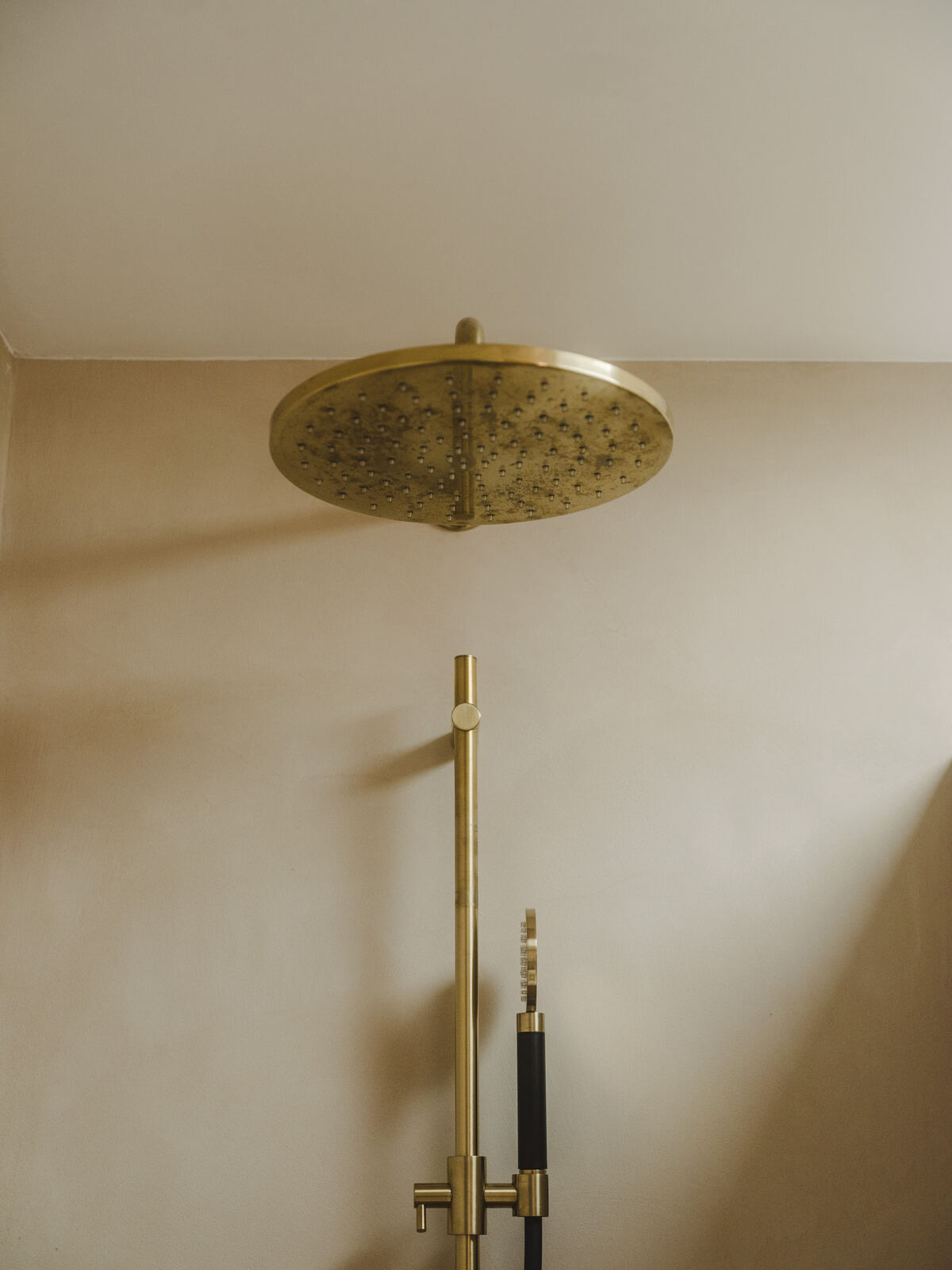 Brass rain shower against soft plaster walls, Casa M