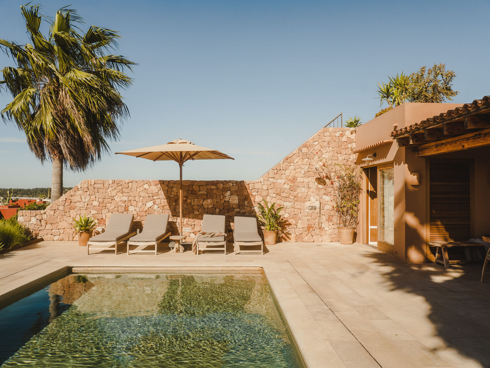 Pool beside a dry stone wall with palm and parasol, Casa M