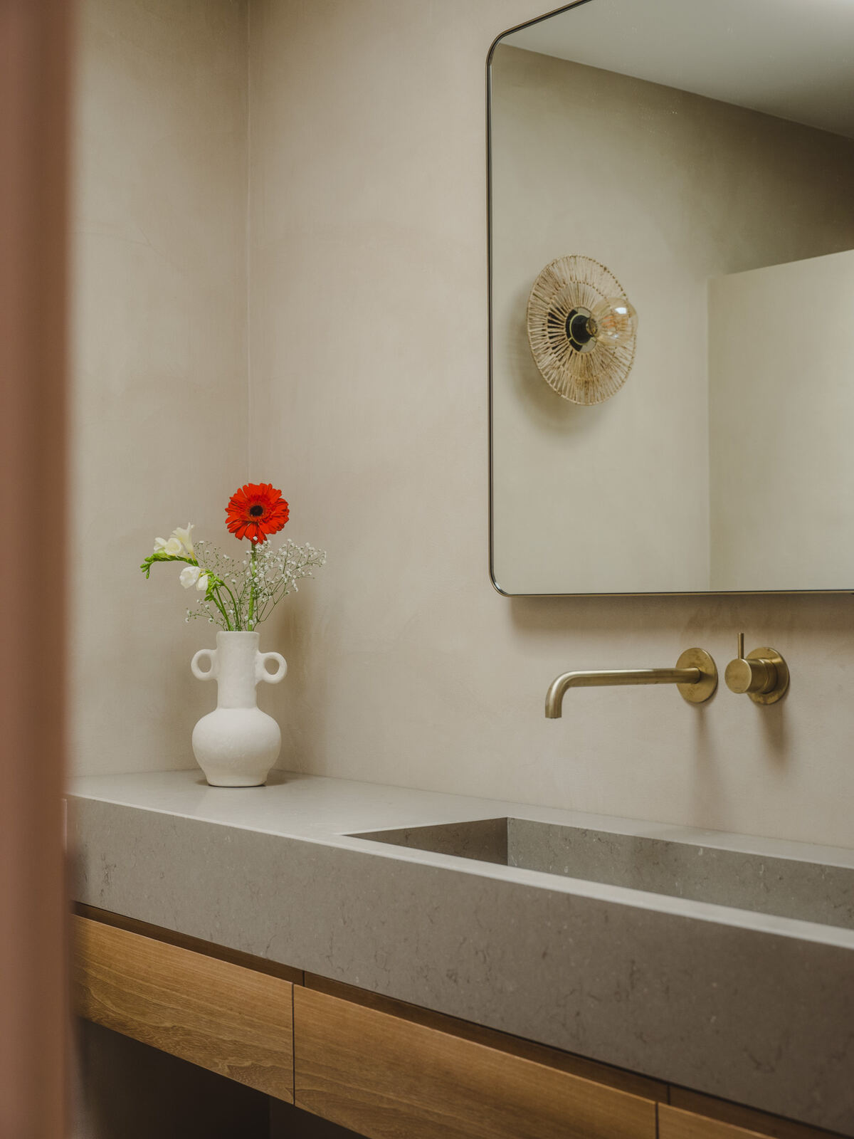 Bathroom vanity in textured stone with mirror and flowers, Casa M