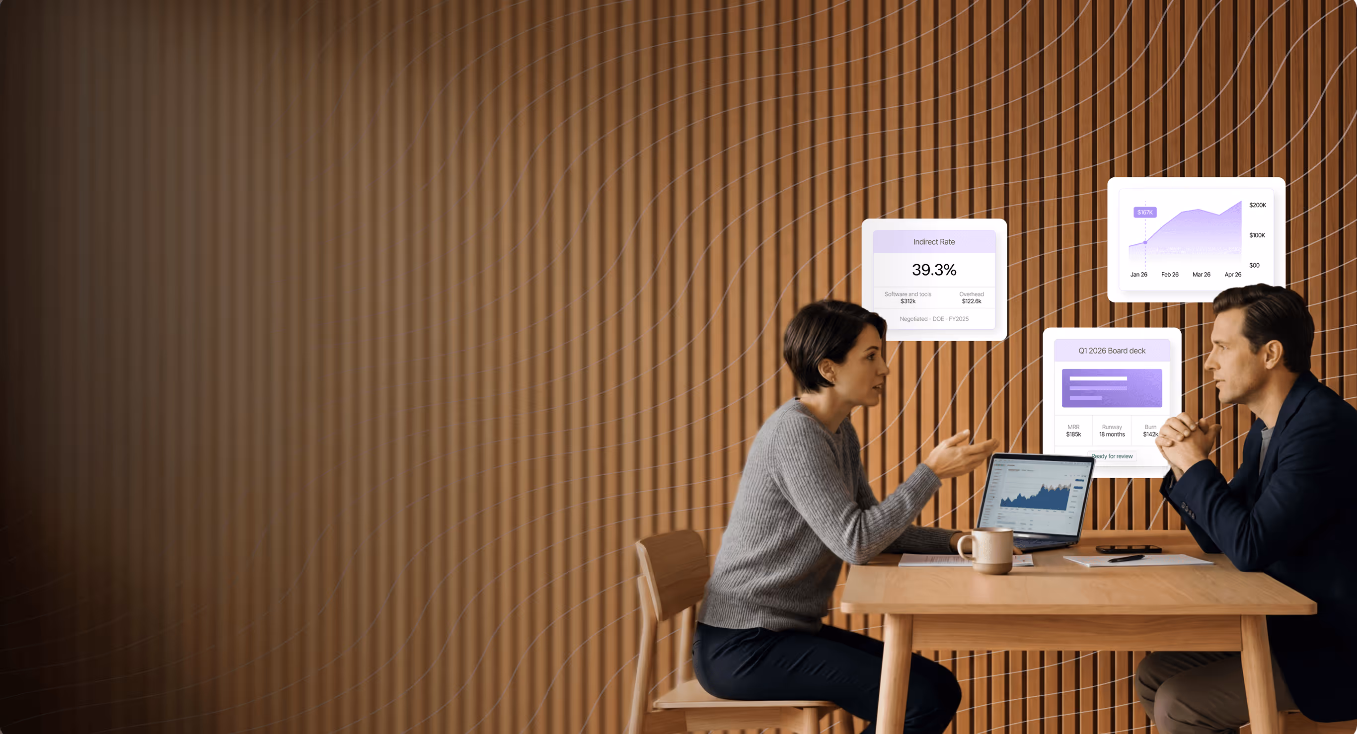 Two people discussing data and graphs displayed above a laptop at a wooden table.
