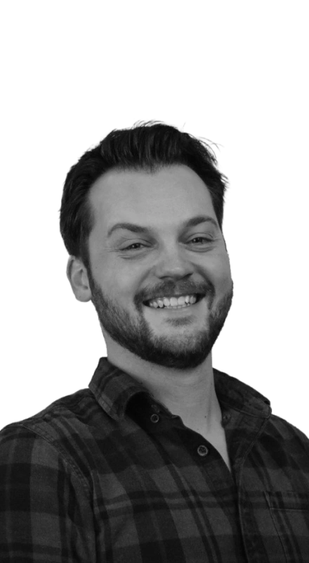 Smiling man with beard, short hair, wearing a checkered shirt in a black-and-white photo.