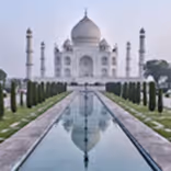 The Taj Mahal with its reflection in the central water canal, framed by four minarets and gardens.