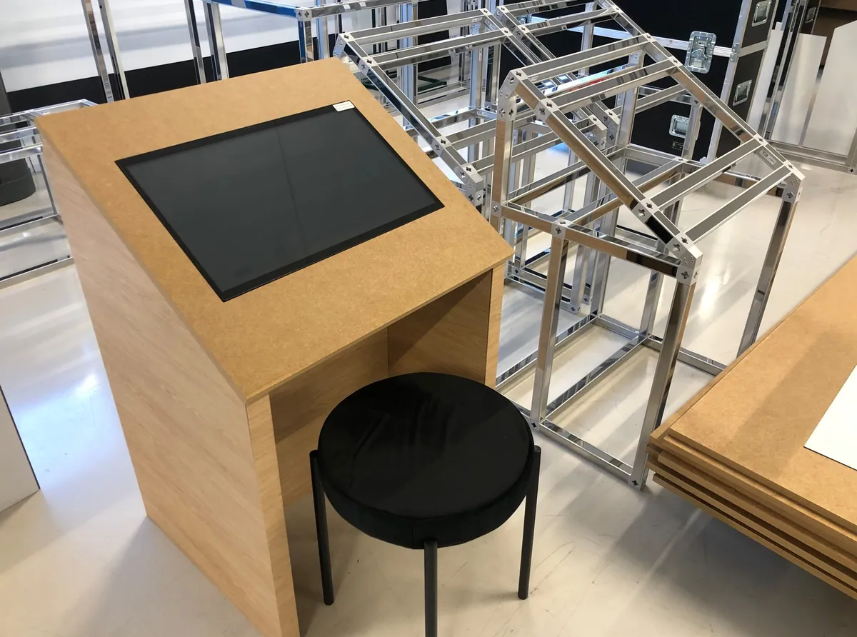 Timber-clad interactive kiosk lectern with touchscreen next to T3 frames