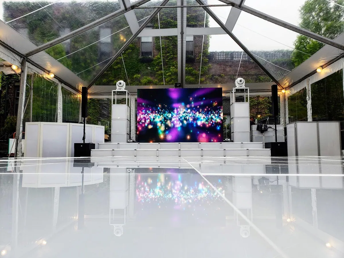White T3 stage and gloss floor inside a glass marquee with LED screen