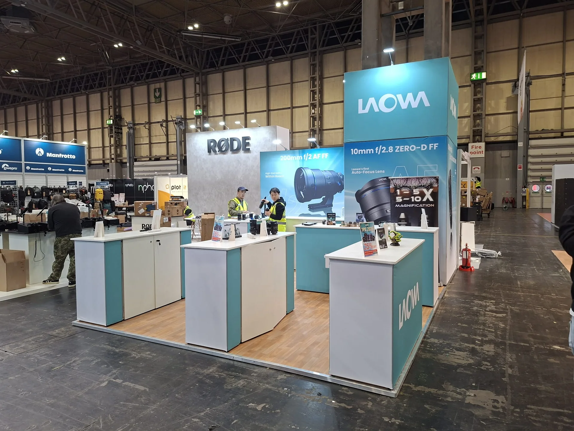 Laowa stand at Photography Show 2026: teal and white stand with display counters of camera lenses on a timber-effect floor