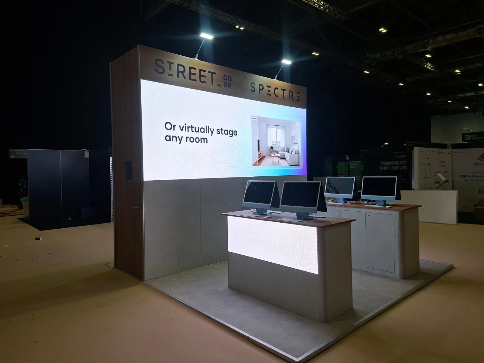 Street stand at Propertymark One 2026: stand with a large backlit screen wall and two counters with monitors on a dark floor