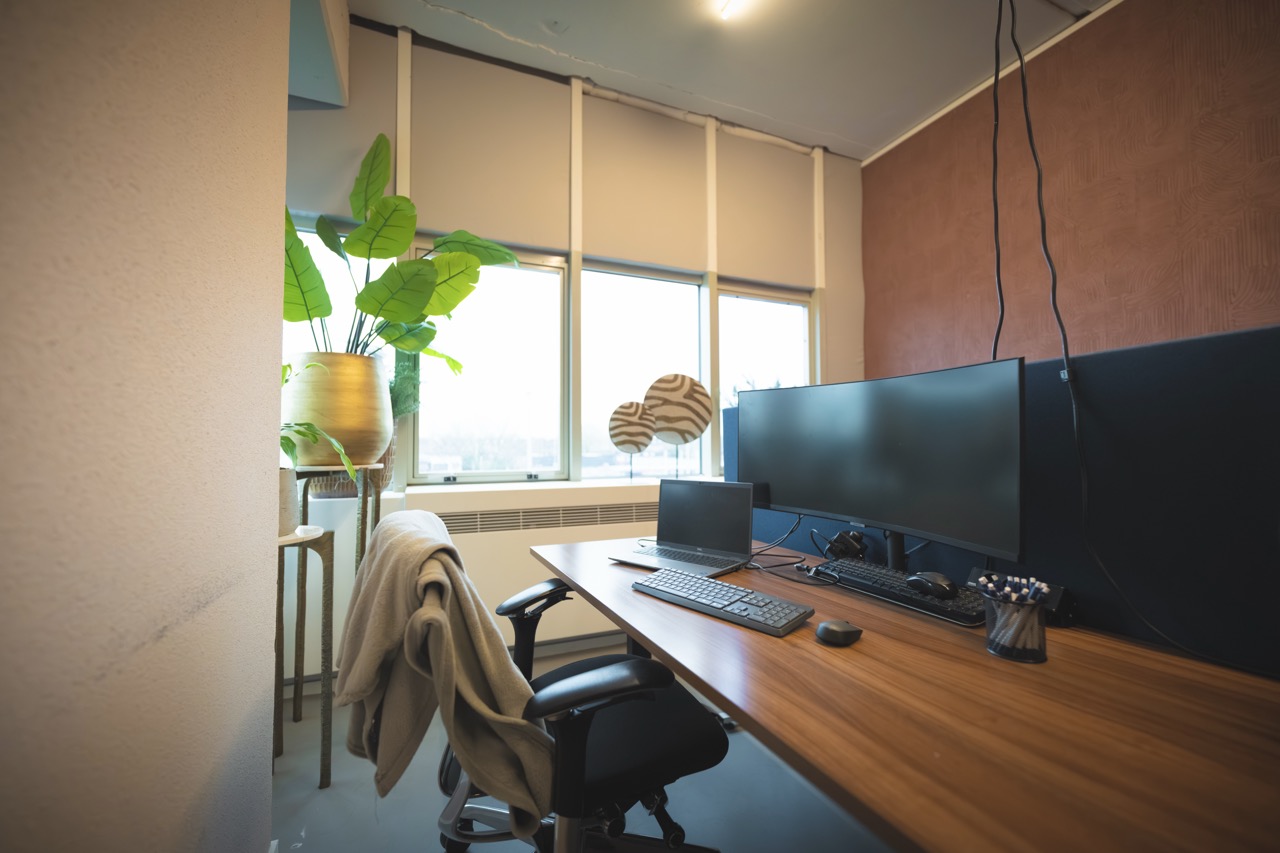 Ingerichte werkplek met een houten bureau, beeldschermen en een plant bij Campus Delta.