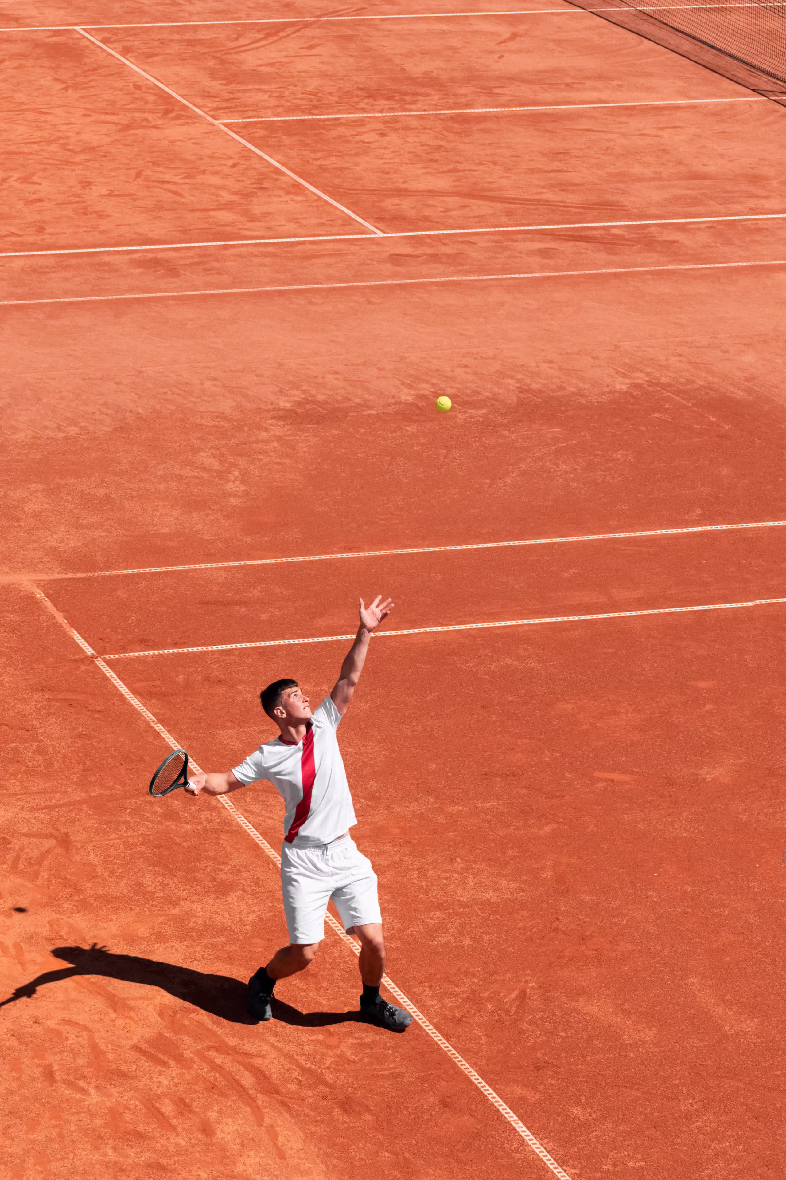 Distant photo of man in white in middle of tennis serve