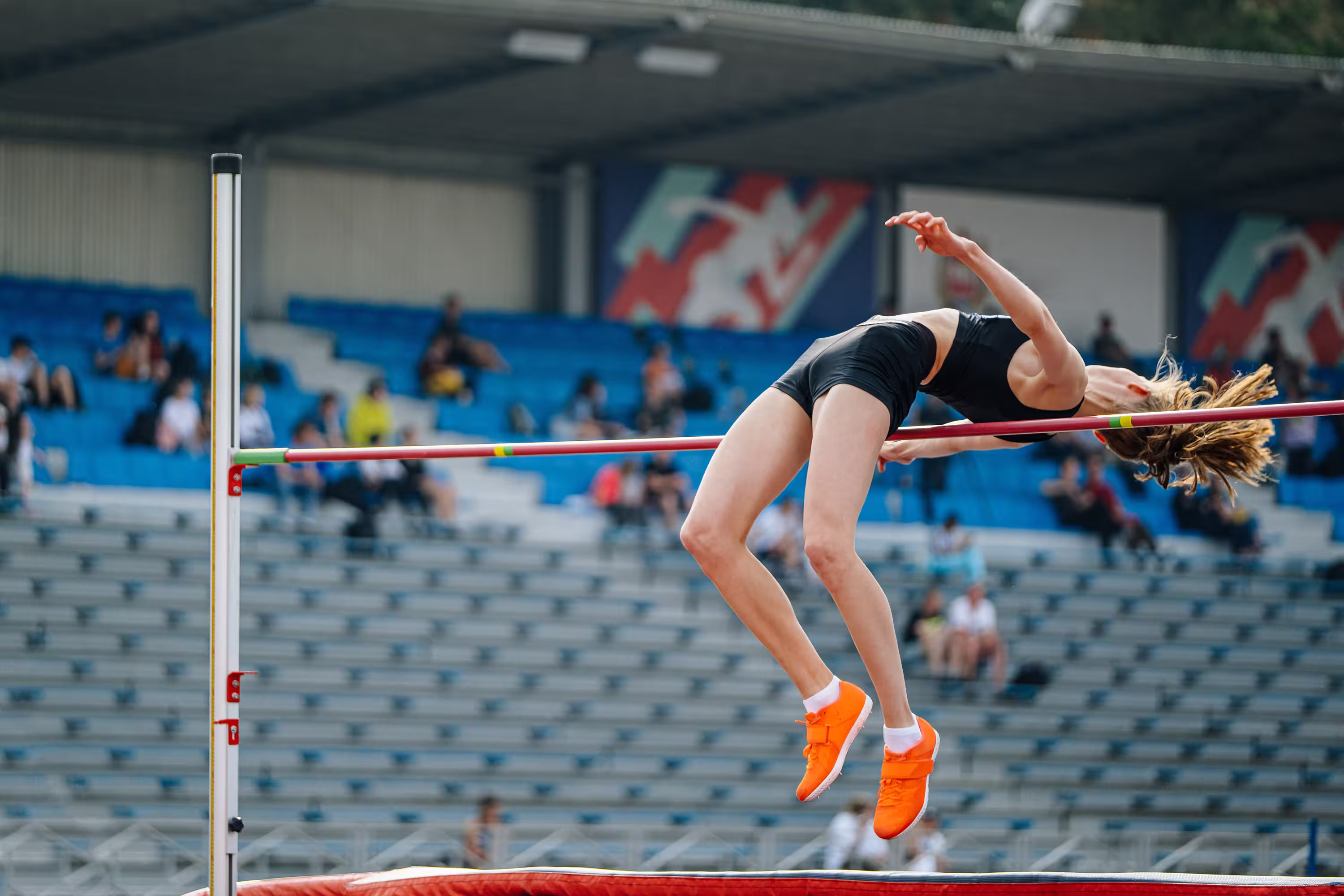 Track athlete lays out and stretches successfully clearing high jump bar