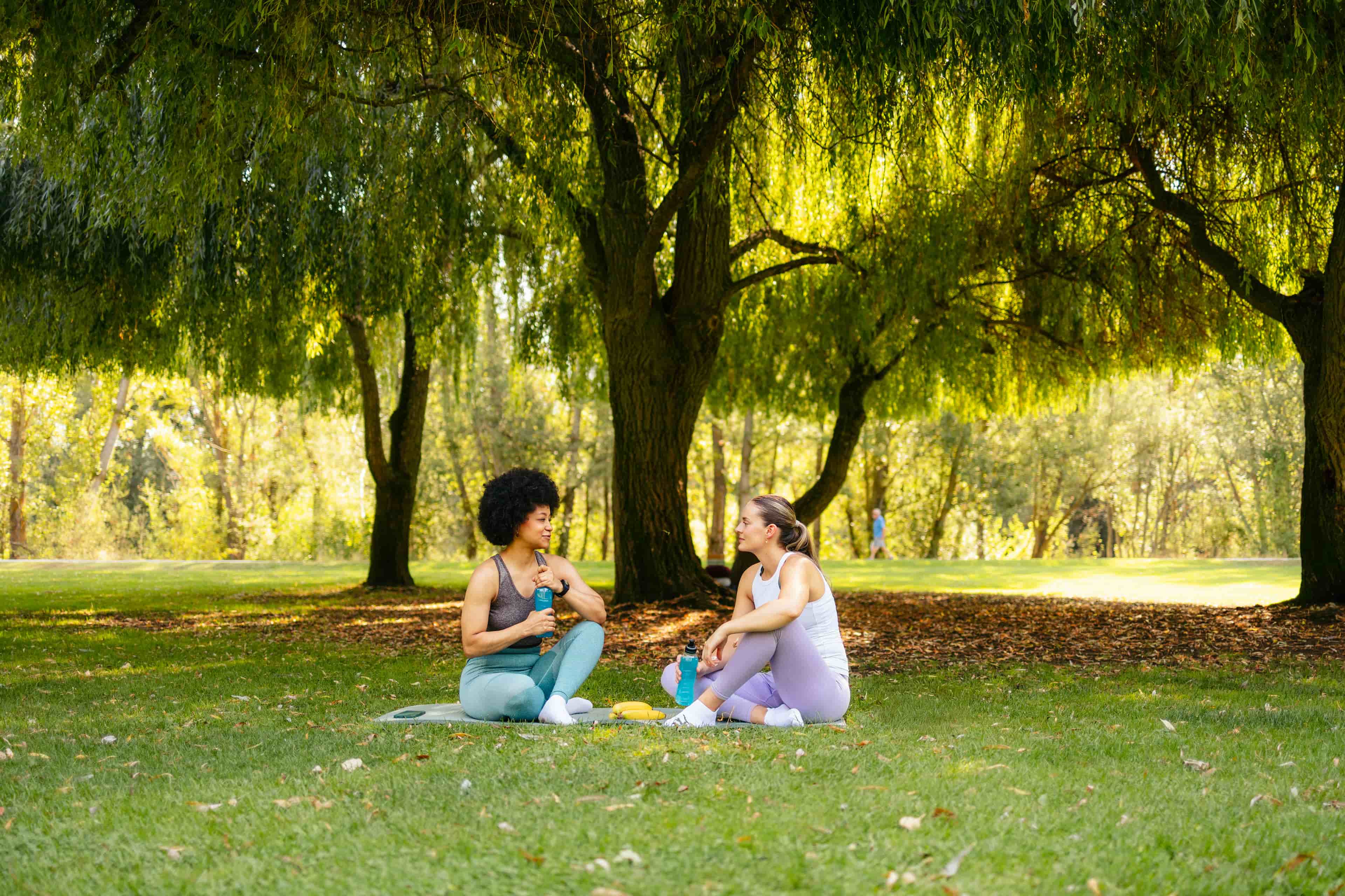 Women happily sitting with friends under tree in yoga clothes