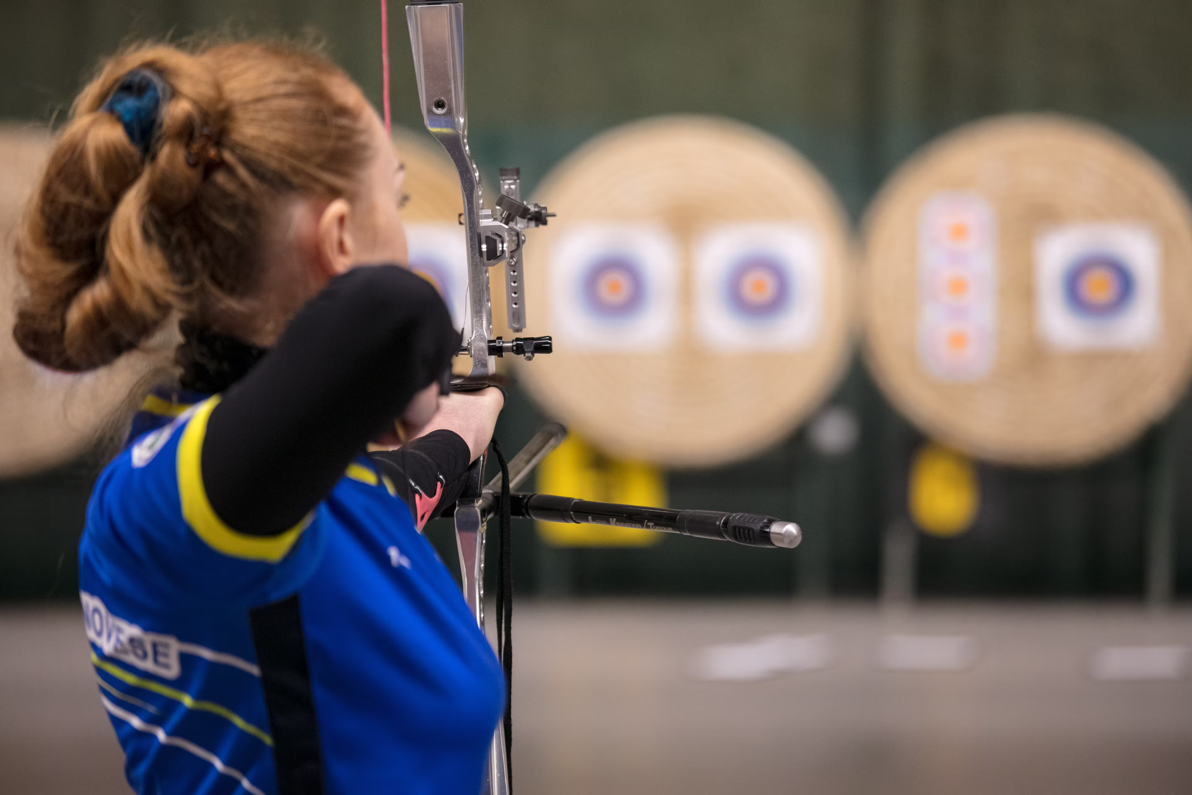 Young woman archer focused aiming at target in distance