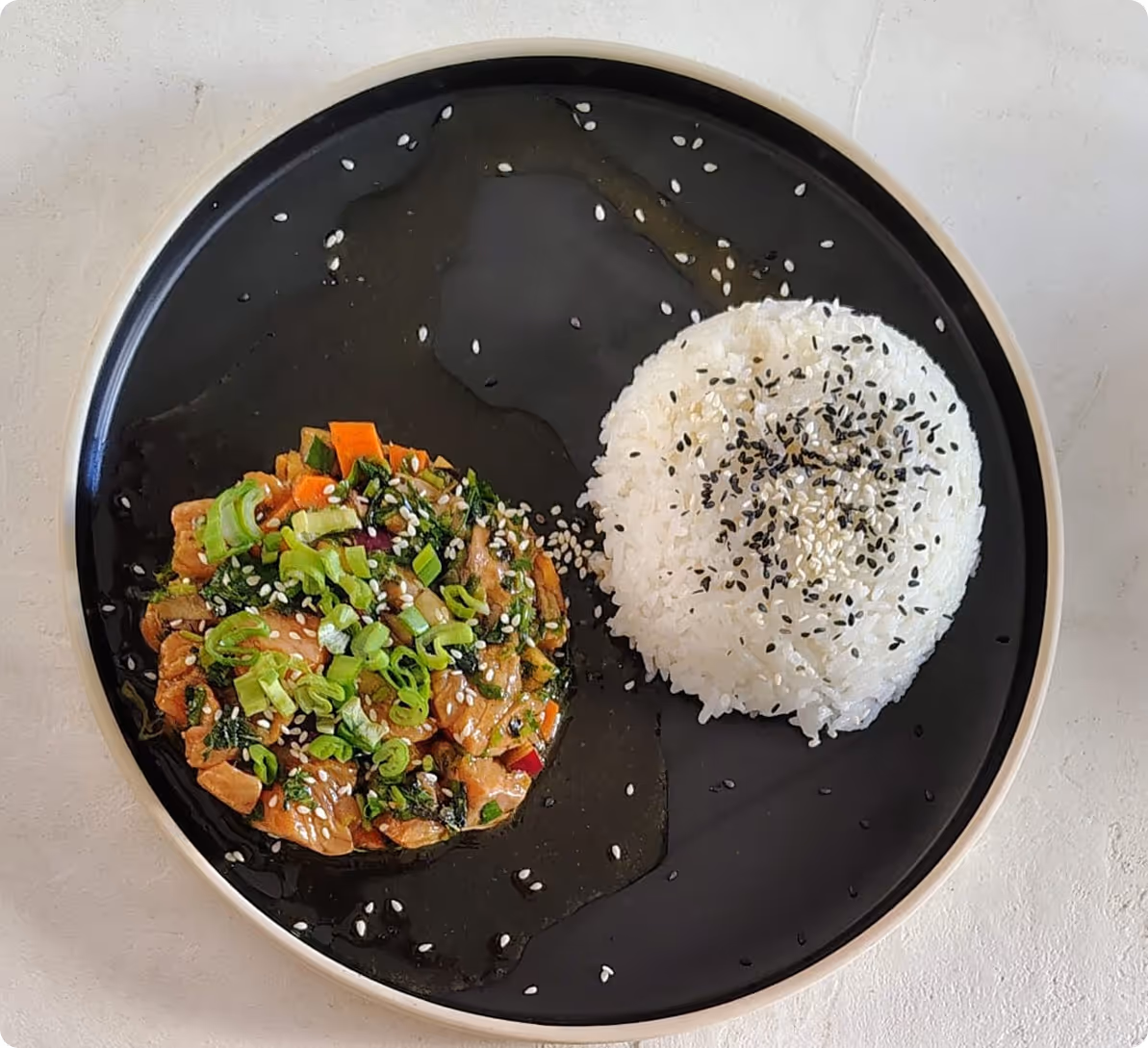 Assiette noire avec une portion de riz blanc parsemé de graines de sésame et un tartare de truite aux légumes.