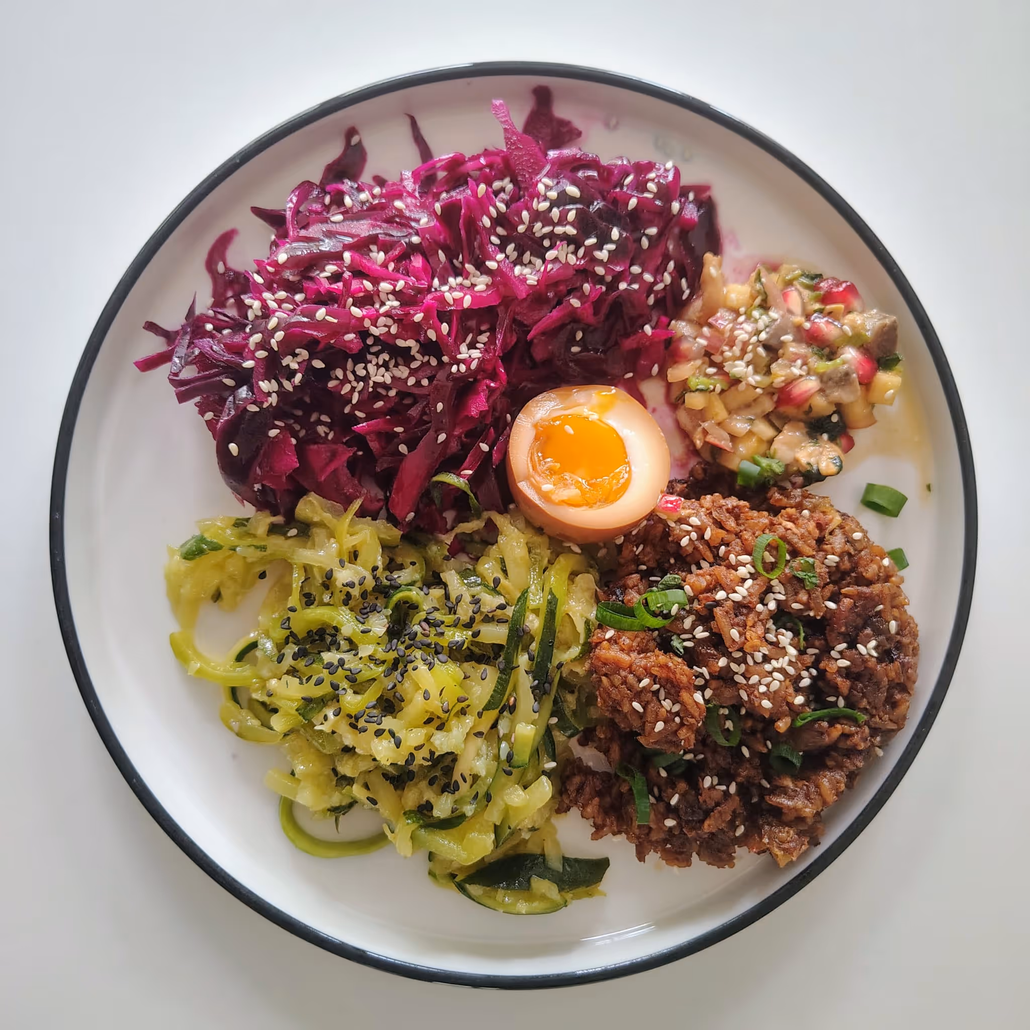 Assiette de salade de chou rouge, riz sauté aux oeufs, oeuf dur, spaghettis de courgettes et ceviche.