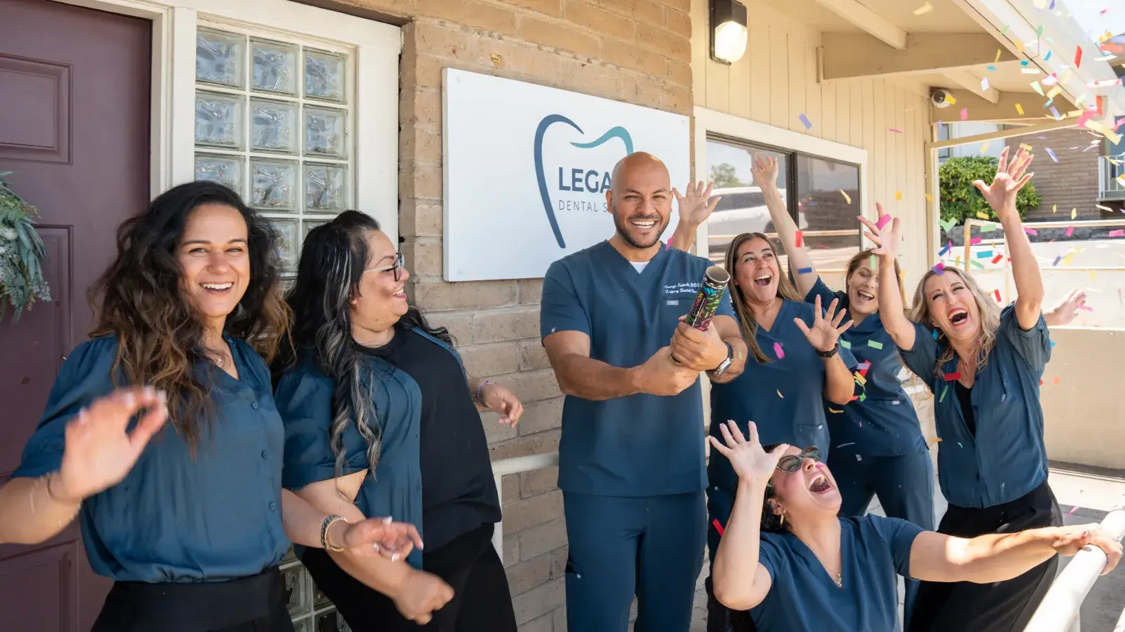 A group of dental clinic staff celebrates with confetti outside their workplace.