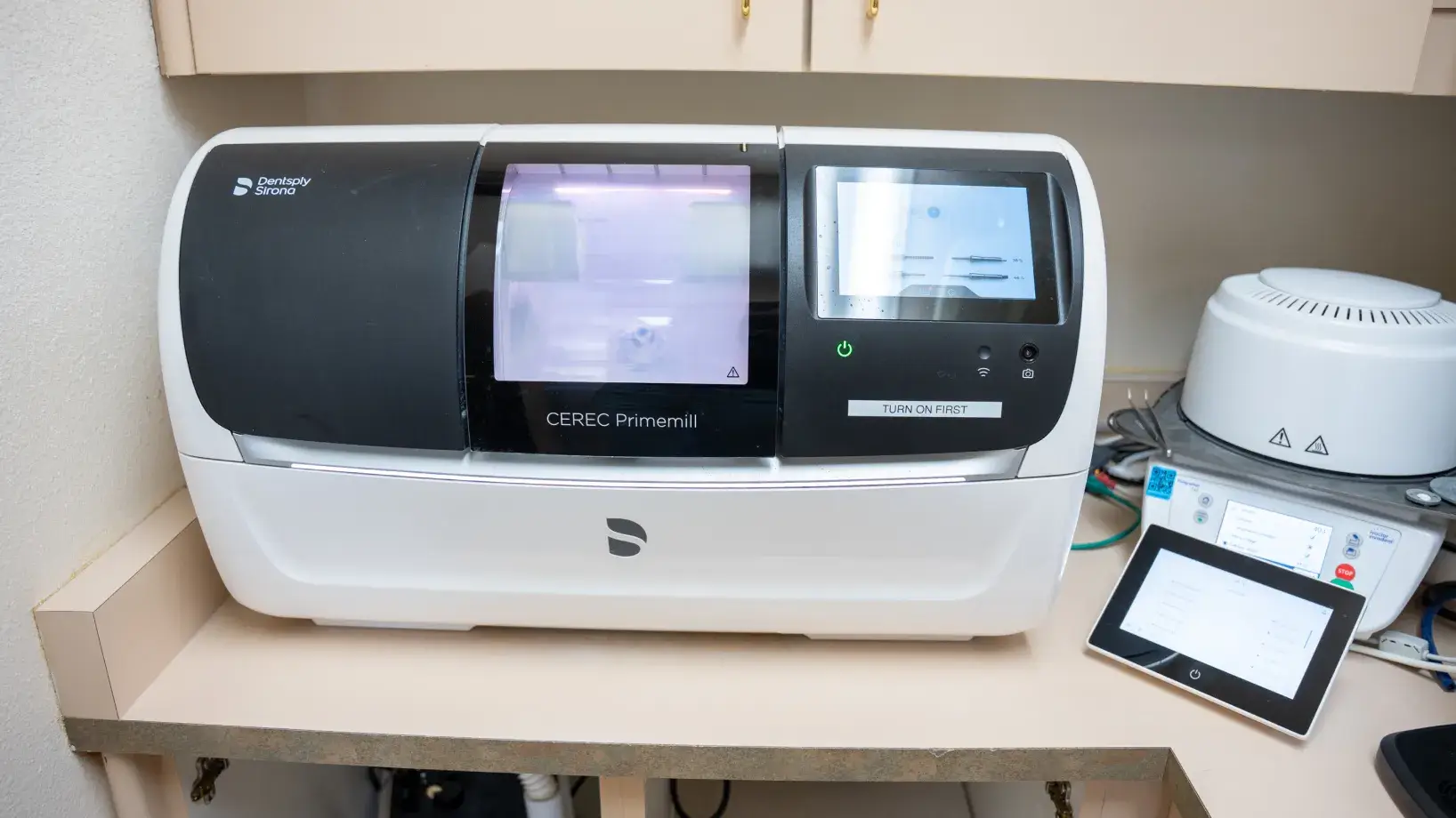 A dental milling machine is placed on a counter, displaying operational settings on its screen.