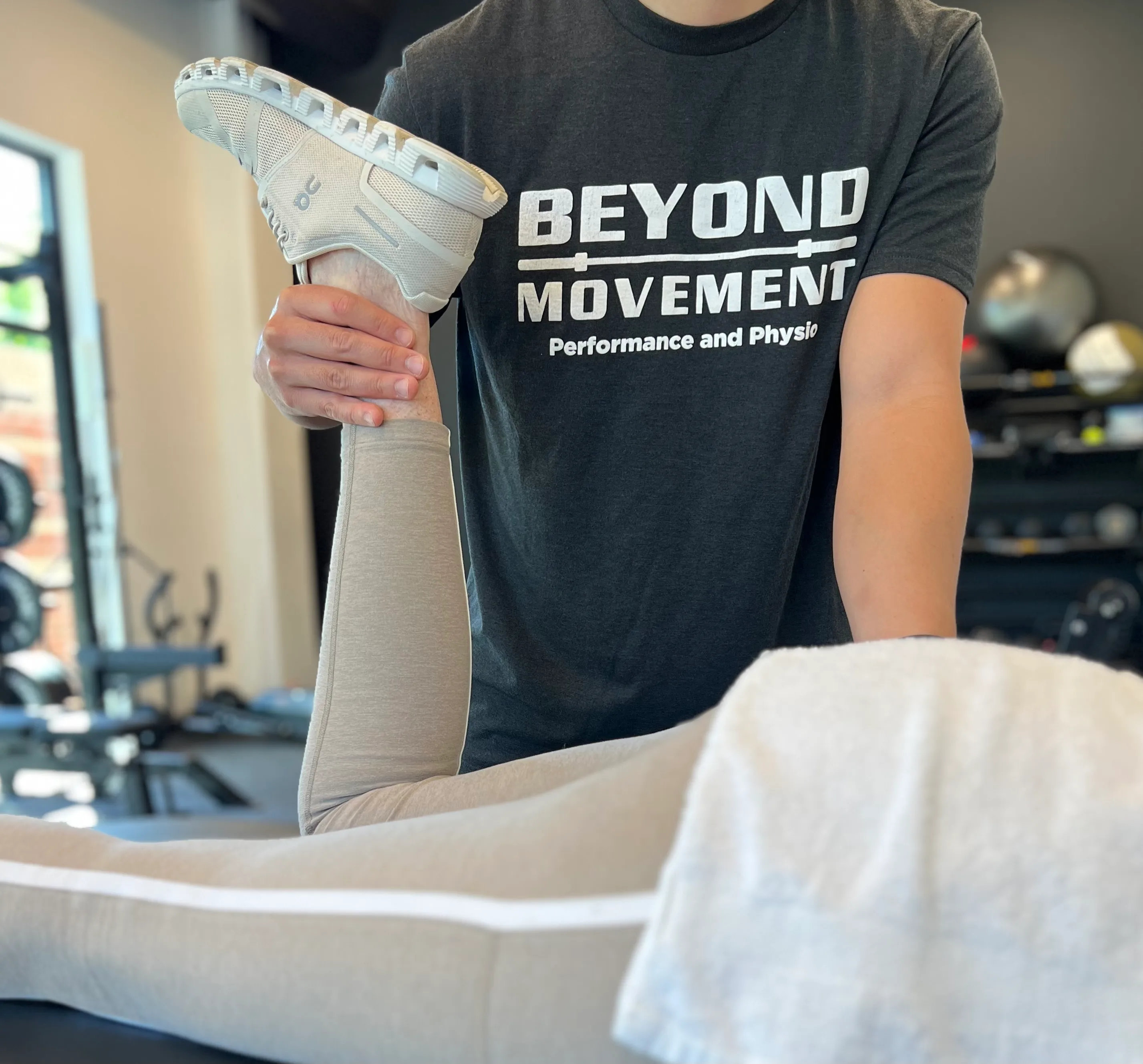 Physical therapist stretching a patient's leg on a treatment table inside a clinic.
