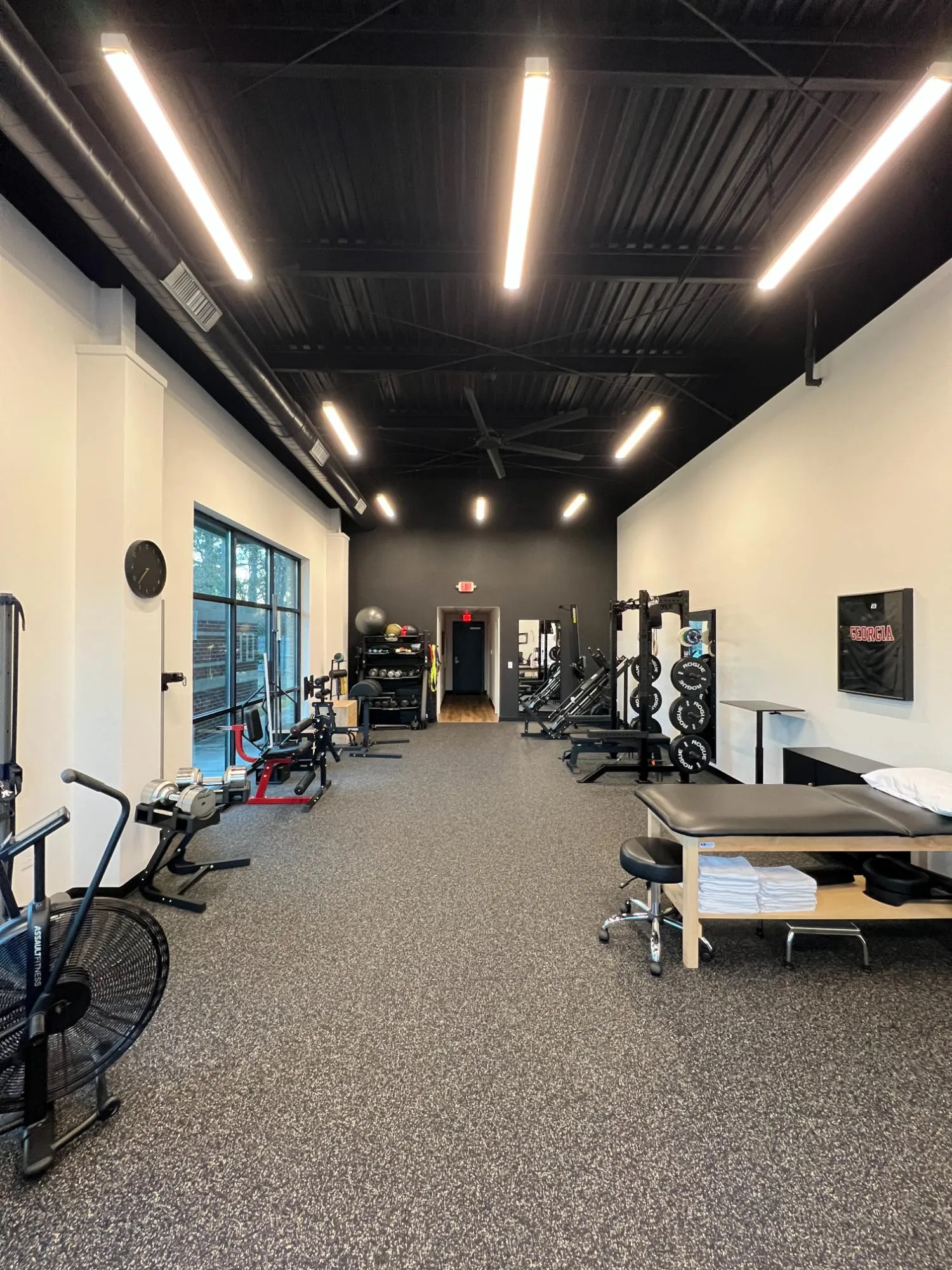 Modern gym with cardio machines, weight racks, exercise balls, and a treatment table with towels.