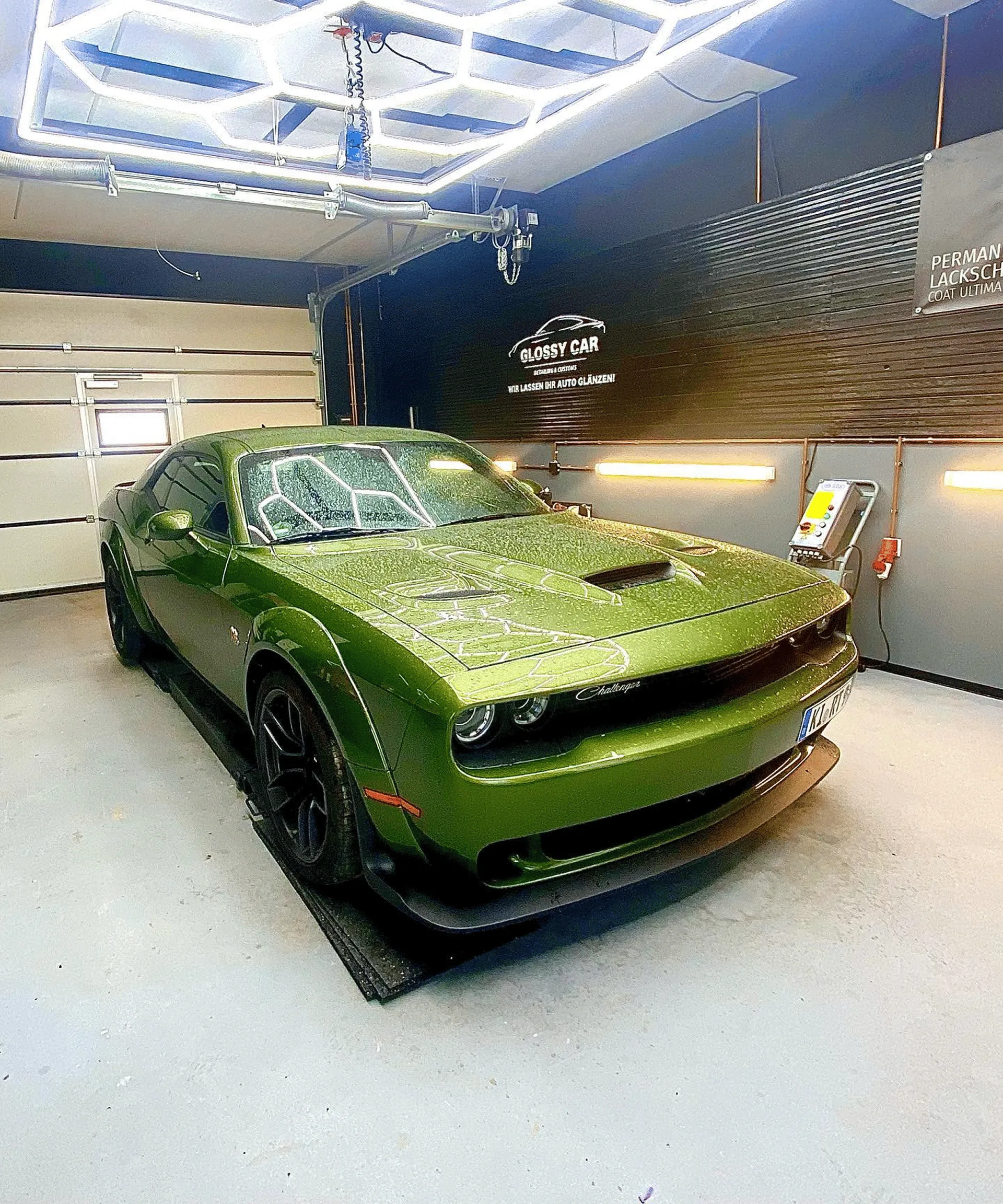 Grüner Dodge Challenger in einer Garage mit reflektierenden Deckenlichtern bei Glanzwerk Autoservice.