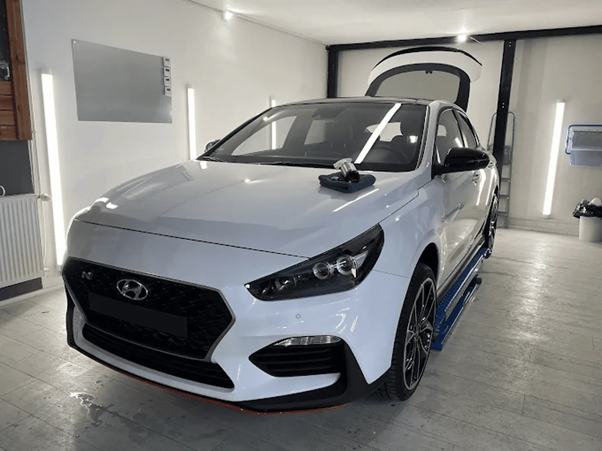 Weißer Hyundai i30 N steht in der Garage von Glanzwerk Autoservice mit geöffnetem Kofferraum, ein Poliergerät liegt auf der Motorhaube.