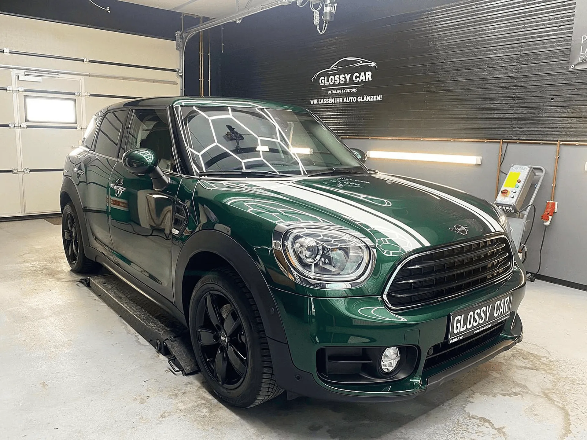 Dunkelgrünes Mini Countryman Auto mit schwarzem Dach und Felgen, in der Glanzwerk Autoservice Werkstatt mit glänzender Oberfläche geparkt.
