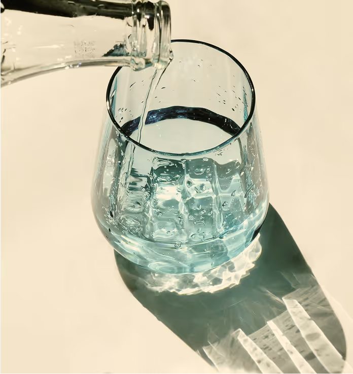 Water being poured from a glass bottle into a textured glass casting a clear shadow on a light surface.