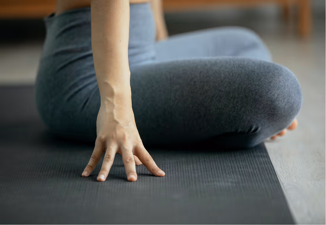 Person sitting cross-legged on a black yoga mat, with one hand resting on the mat.