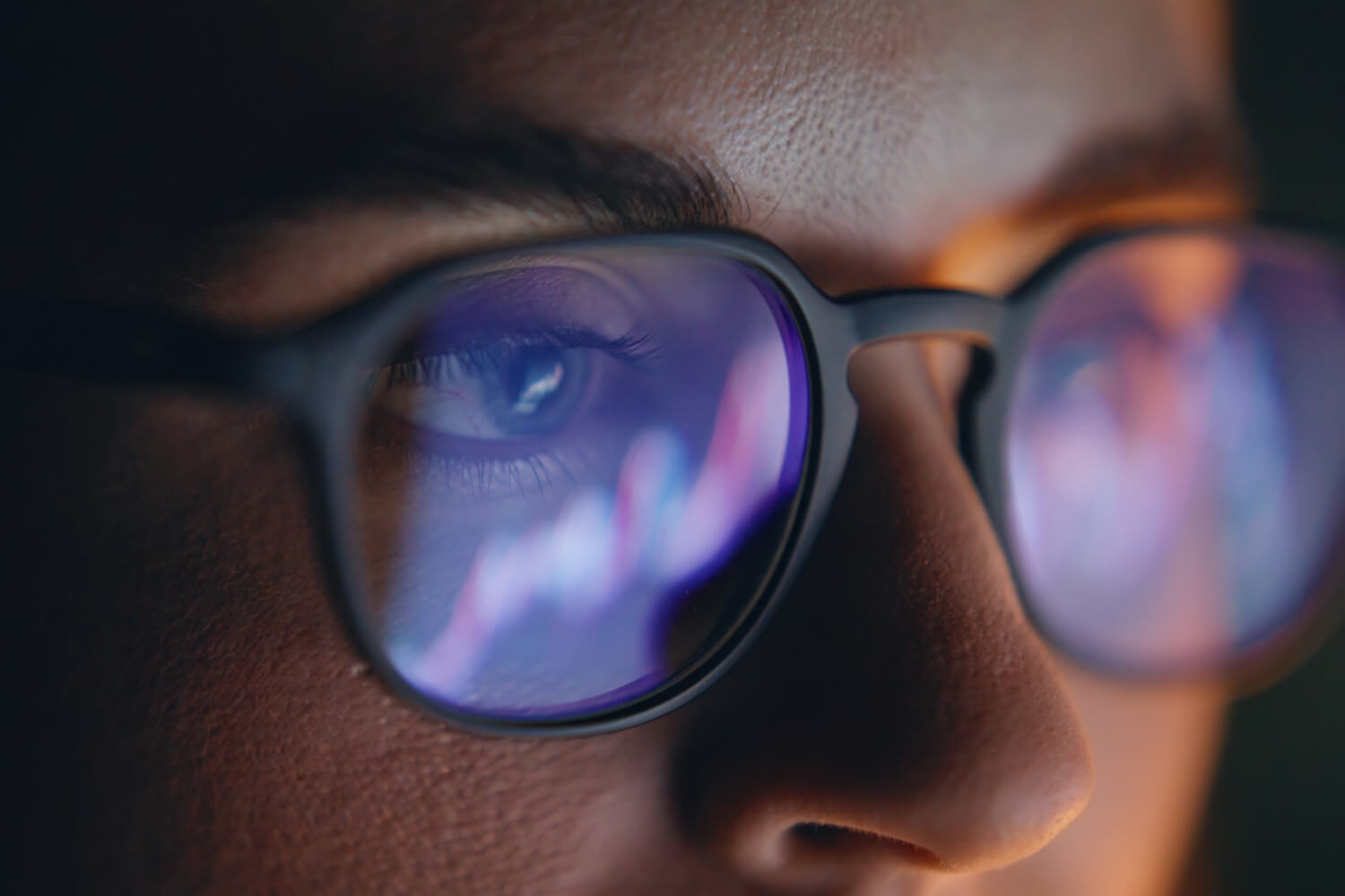 Reflections of financial data charts visible on the lenses of a person's glasses.