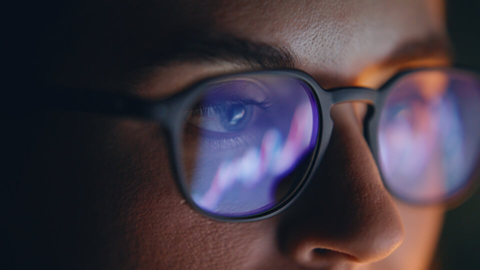 Reflections of financial data charts visible on the lenses of a person's glasses.