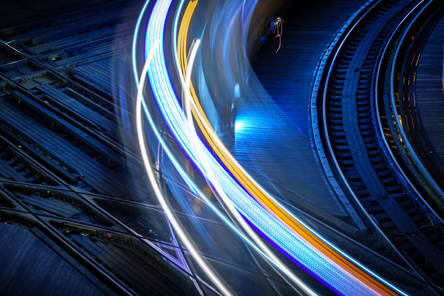 Long-exposure light trails curving across railway tracks at night.