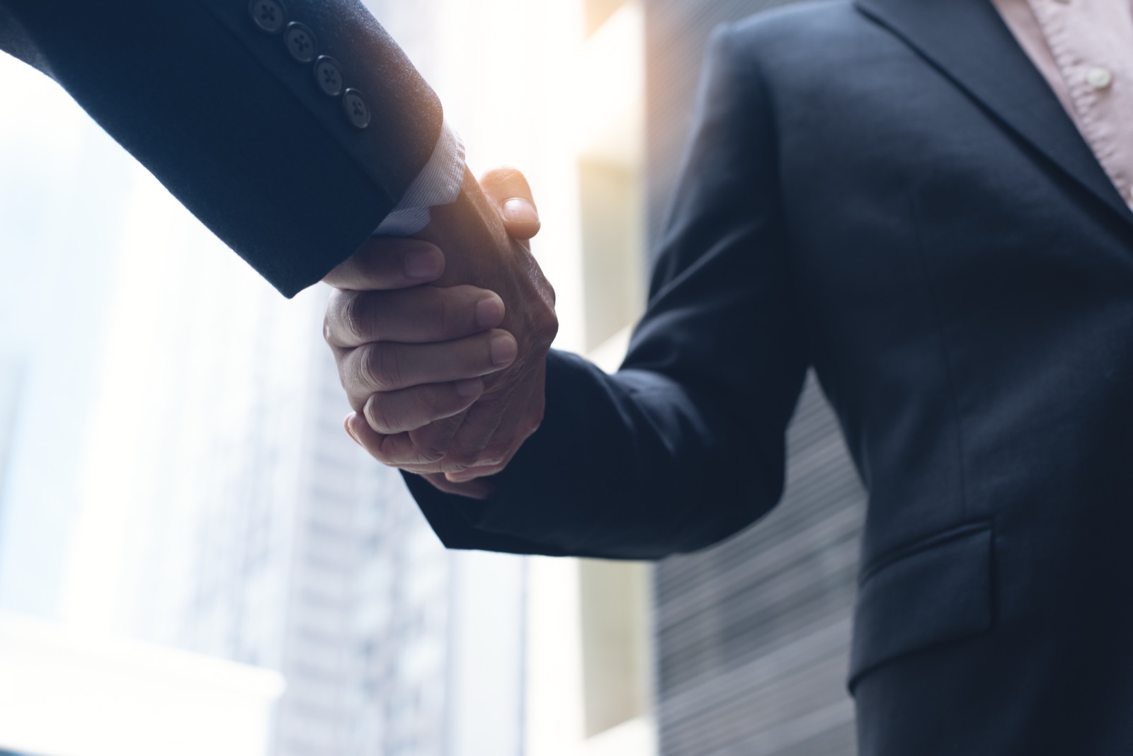Two business executives shaking hands outdoors, signaling an agency merger deal