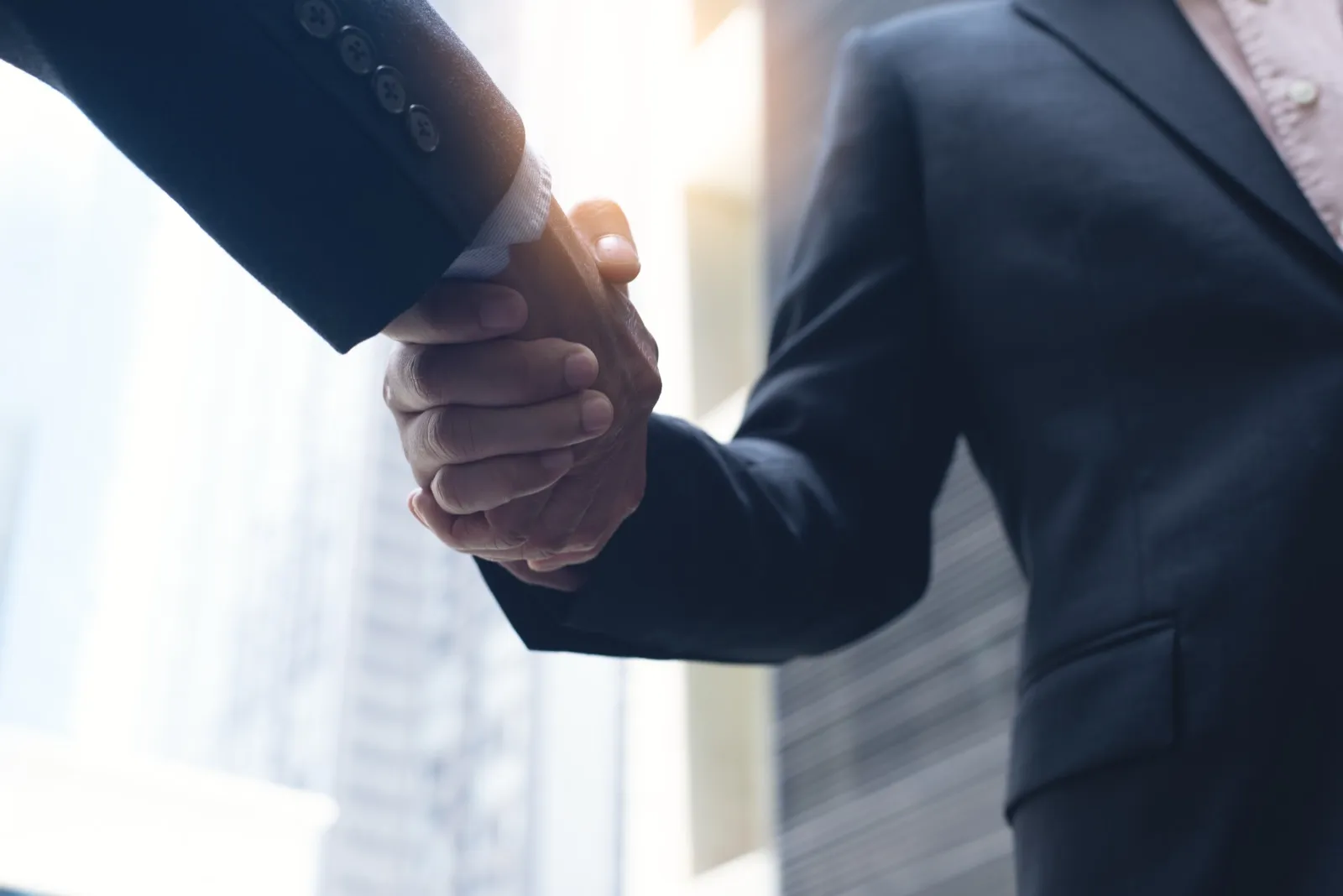 Two business executives shaking hands outdoors, signaling an agency merger deal