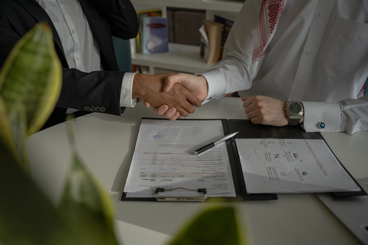 Two professionals shaking hands over signed financial documents