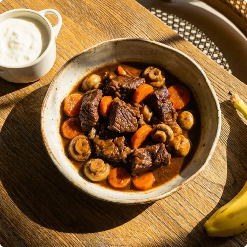 Plat de bœuf mijoté avec carottes et champignons dans un bol sur une table en bois.