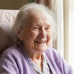 Femme âgée souriante assise près d'une fenêtre avec lumière naturelle