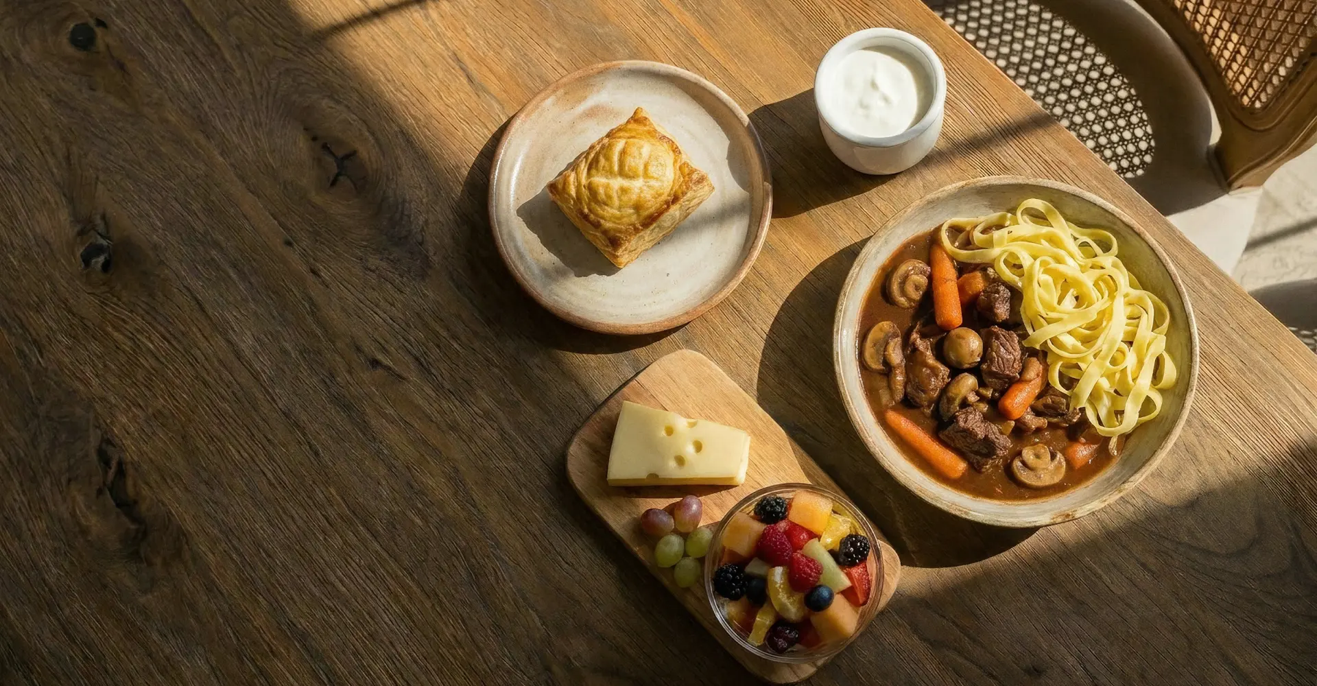 Repas avec ragoût de bœuf aux champignons, pâtes, tartelette, fromage, fruits et crème.