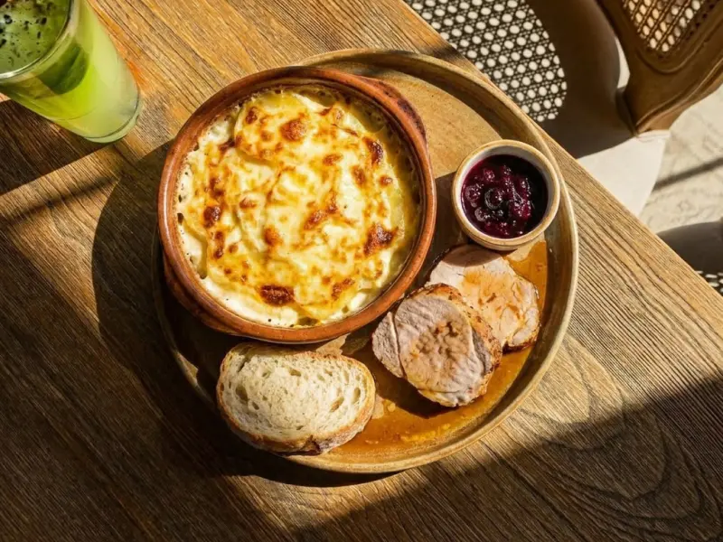 Plat gratiné avec tranches de pain, viande et sauce aux baies sur une table en bois.