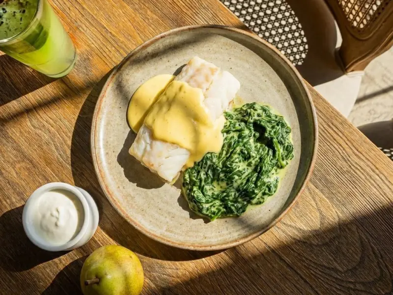 Plat avec filet de poisson blanc nappé de sauce et épinards à la crème sur une assiette beige.