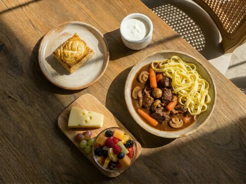 Plat avec bœuf, champignons, carottes, pâtes, accompagné de tarte, fromage, fruits et yaourt.