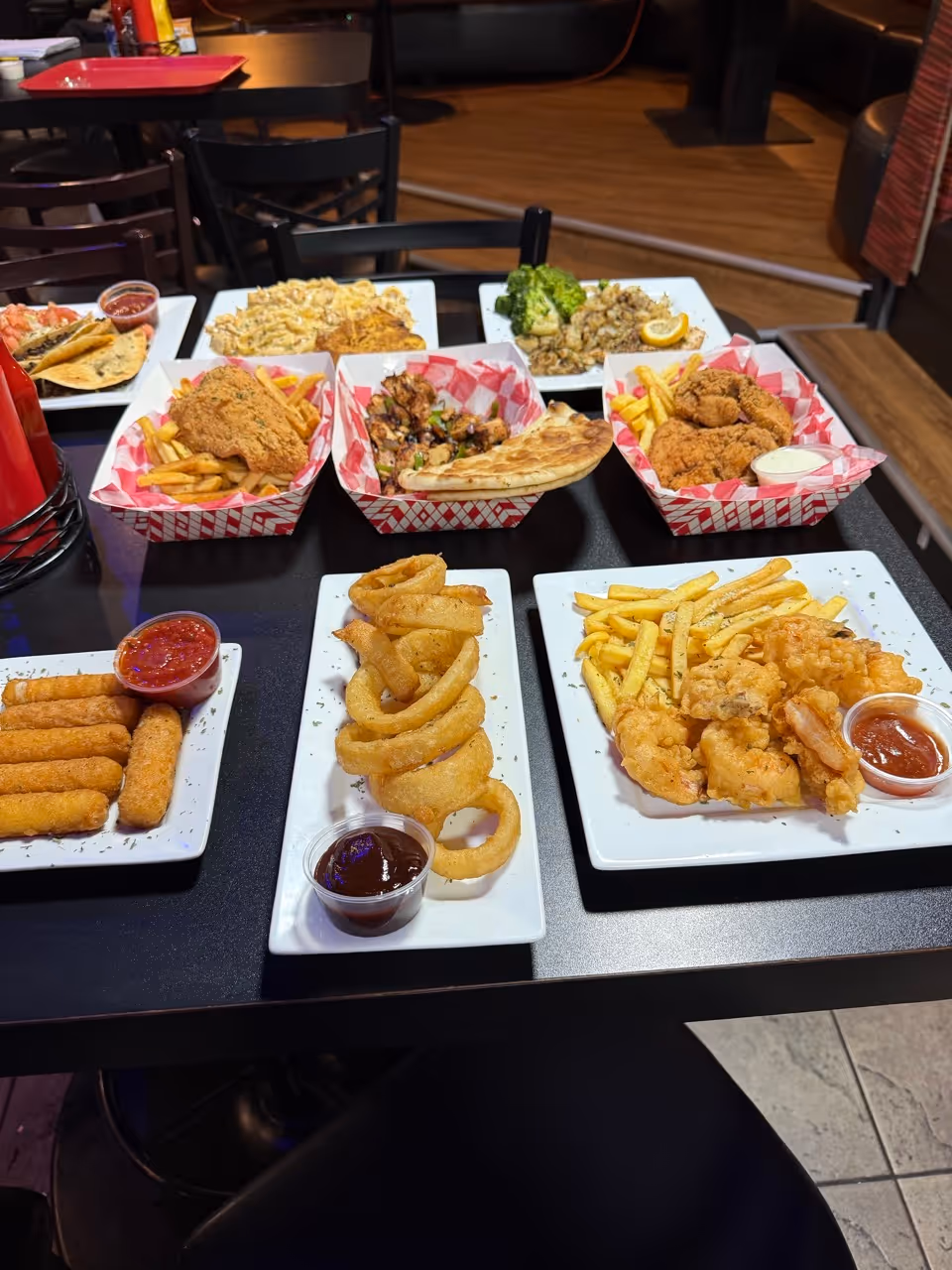 table with different type of dishes, like onion rings, mozzarella sticks, fried chicken fries and more