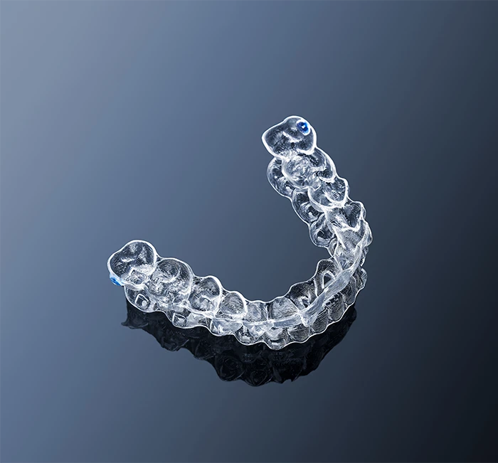 Clear dental aligner resting on a glossy, dark reflective surface.