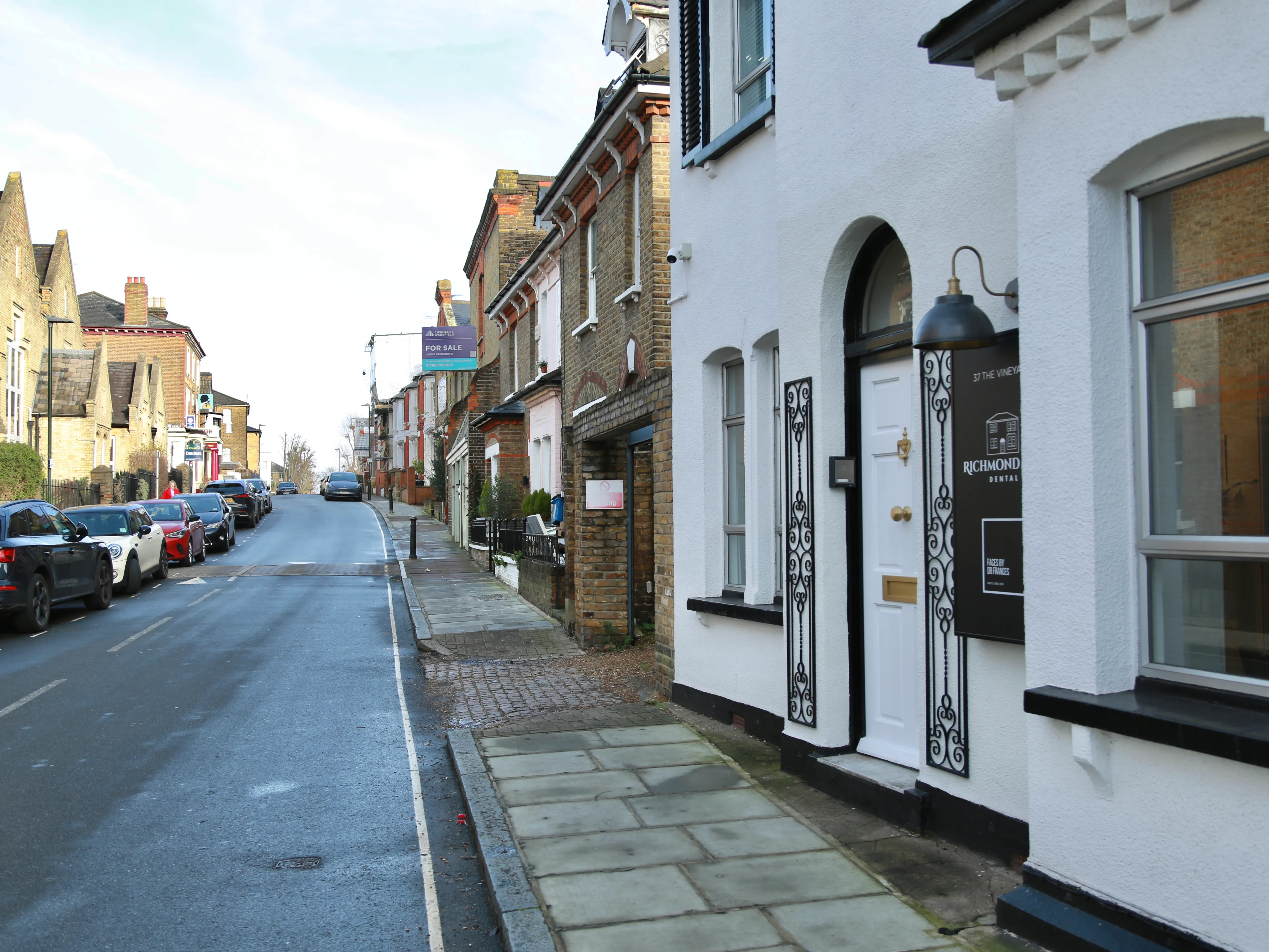 Street view of parked cars and brick houses with a white building showing Richmond Dental sign.