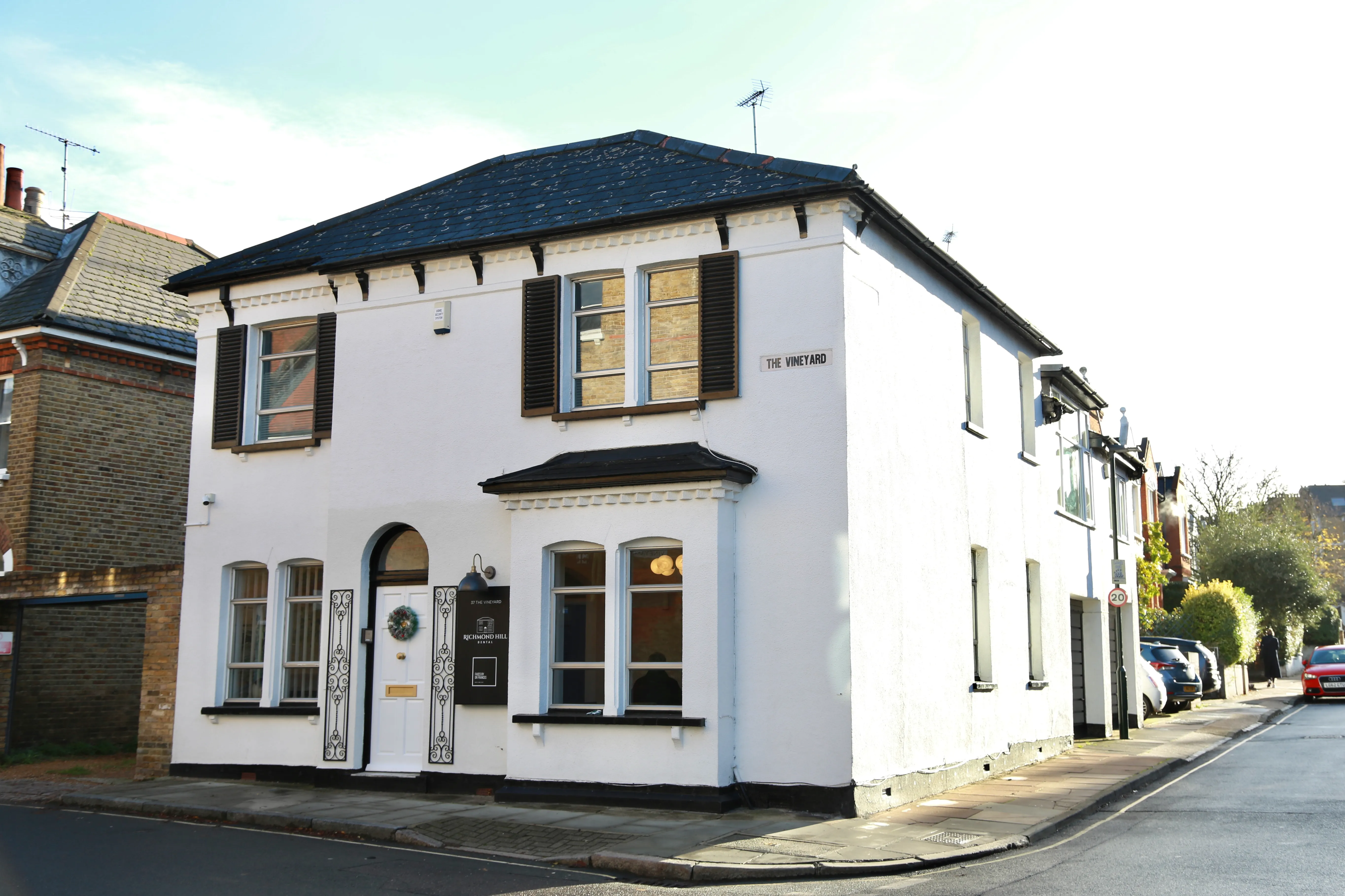 White two-story building with black shutters and a sign reading The Vineyard on a sunny street corner.