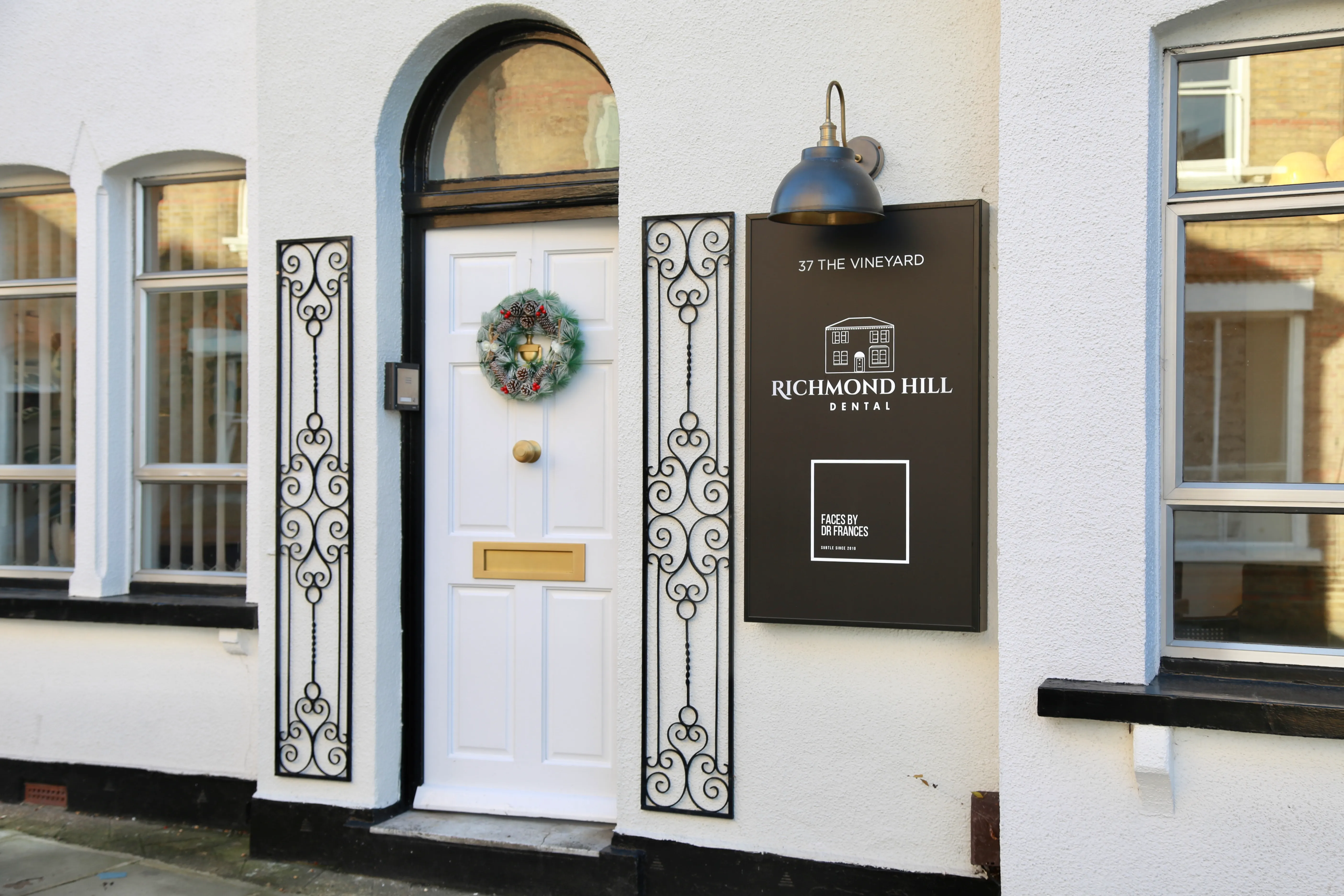 White door with holiday wreath at Richmond Hill Dental office with black sign and decorative iron panels.