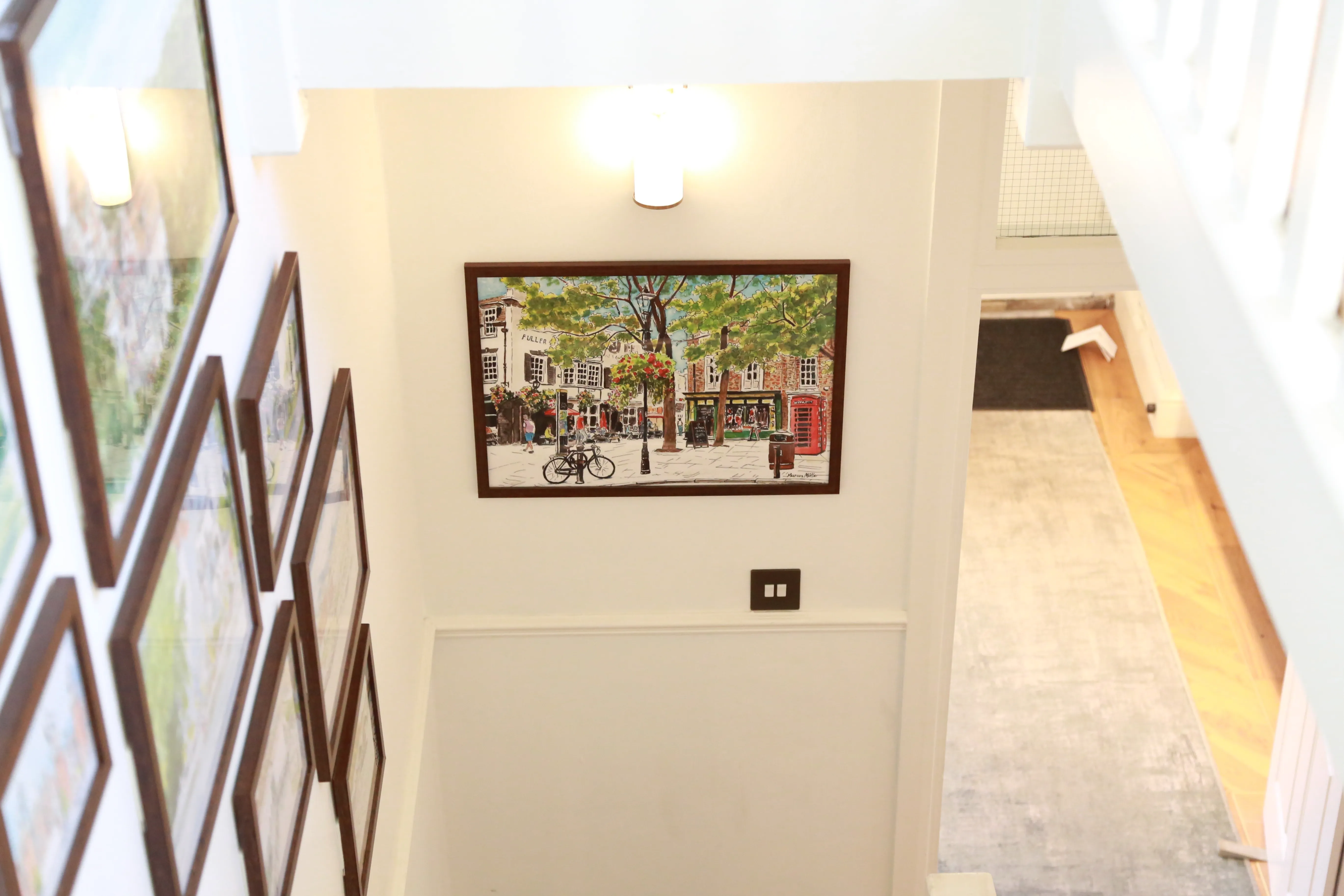 Framed paintings decorating white walls along a stairway in a bright home interior.